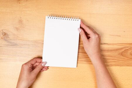 Woman hand holding blank paper on wooden background.