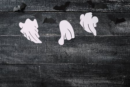 White ghost costume on dark black wooden background. Minimalistic Halloween concept. craft paper ghostsの写真素材