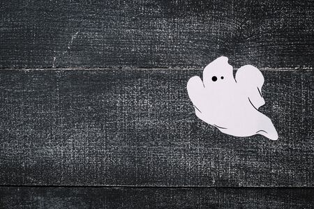 White ghost costume on dark black wooden background. Minimalistic Halloween concept. craft paper ghostsの写真素材