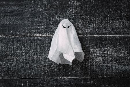 White ghost costume on dark black wooden background. Minimalistic Halloween concept. craft paper ghostsの写真素材