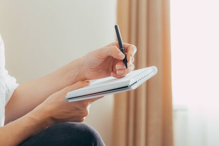 Beautiful female hands are holding an open book or magazine in a room on against a light wallの写真素材
