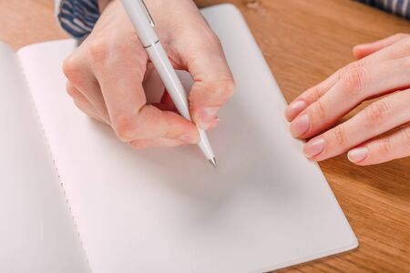 Beautiful Female hands write pen in a notebook of tasks and goals to work on a  tableの写真素材