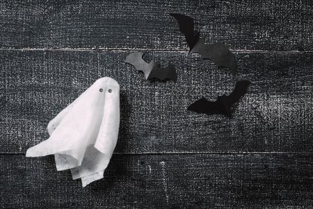 White ghost costume on dark black wooden background. Minimalistic Halloween concept. craft paper ghostsの写真素材