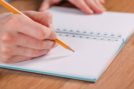 Close up of woman's hands writing in spiral notepad placed on wooden desktop