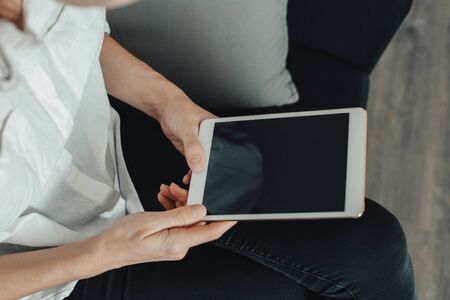 Mockup image of a woman sitting and holding white tablet pc with blank desktop screen