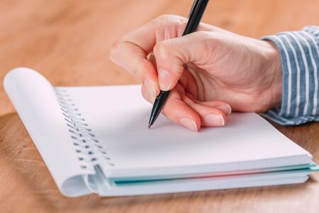Close up of woman's hands writing in spiral notepad placed on wooden desktop