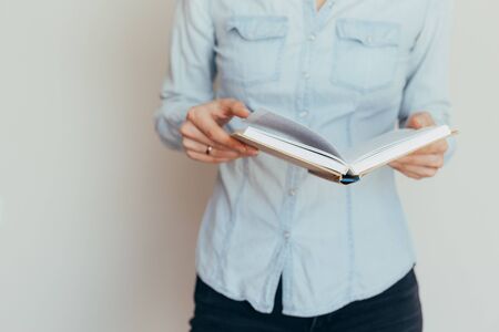 Beautiful female hands are holding an open book or magazine in a room on against a light wall