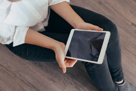 Mockup image of a woman sitting and holding white tablet pc with blank desktop screenの写真素材