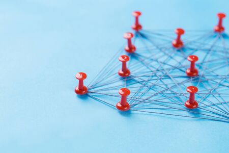 network with red and white pins and string, An arrangement of colorful pins linked together with string on a blue background suggesting a network of connections.の写真素材
