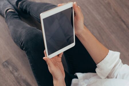 Mockup image of a woman sitting and holding white tablet pc with blank desktop screen 