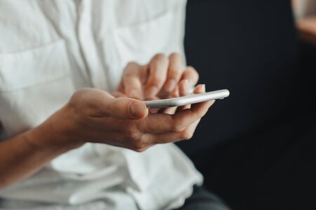 Woman hand holding white mobile phone and sitting on black sofa at home.の写真素材