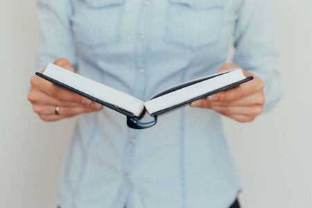 Beautiful female hands are holding an open book or magazine in a room on against a light wall