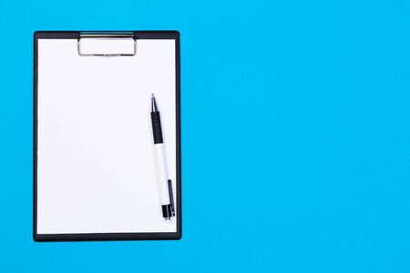 Clipboard with white sheet and pen on a colored background. View from above. space for text