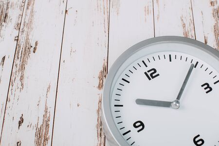 minimalist white wall clock with light metal on wooden background textureの写真素材