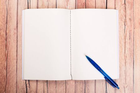 Empty paper notebook on brown wooden table background. Top view Concept of a new workplace of office...
