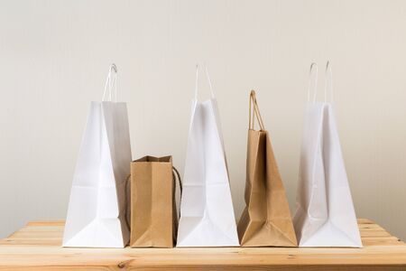 An empty paper bag with handles for shopping, on the front right side of a table in light wood with...