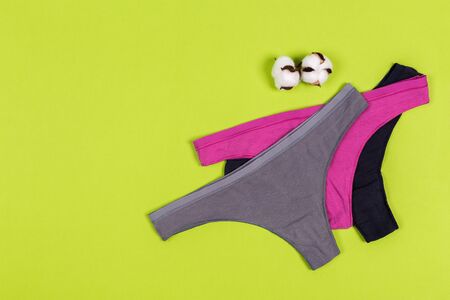 Female pastel cotton set panties and cotton flower on green background top view flat lay with copy space for text. Fashion blog, Colorful women's natural underwear, advertising, shopping concept.の写真素材