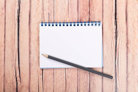 Empty paper notebook on brown wooden table background. Top view Concept of a new workplace of office...