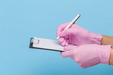 female hand in a pink medical glove holds a blank form of paper on a blue background. Mock up,...