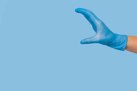 Doctor's hand in a blue medical glove holds an object on a blue background.  mocap, you can insert your product for advertisingの写真素材