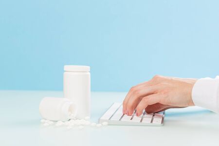 doctor's hands in a white medical coat are typing on the keyboard, two white cans with pills and a red heart. concept of medicine, cardiologyの写真素材