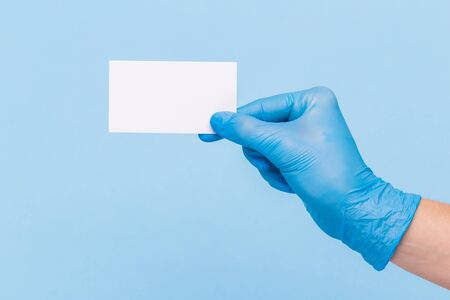 female hand in a sterile medical glove holds a blank form of paper on a blue background. Mock up, business card, flyerの写真素材