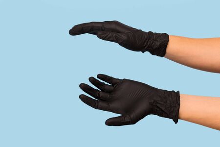 hand in a black medical glove holds an object on a blue background. Mock up, you can insert your...