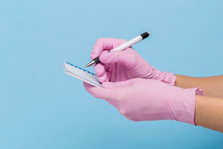 female hand in a pink medical glove holds a blank form of paper on a blue background. Mock up, business cardの写真素材
