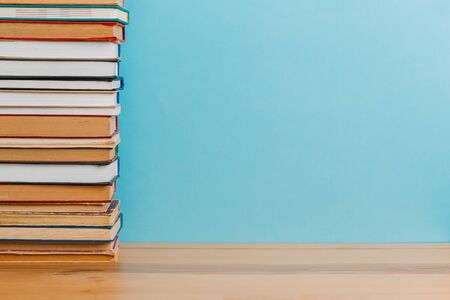 A simple composition of many hardback books, raw books on a wooden table and a bright blue...