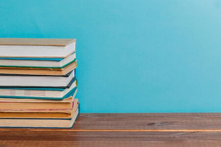A simple composition of many hardback books, raw books on a wooden table and a bright blue...