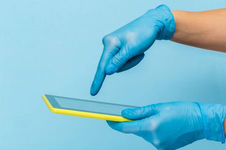 Female hand in a  medical glove holds a blank modern tablet on a blue background. Mock up.