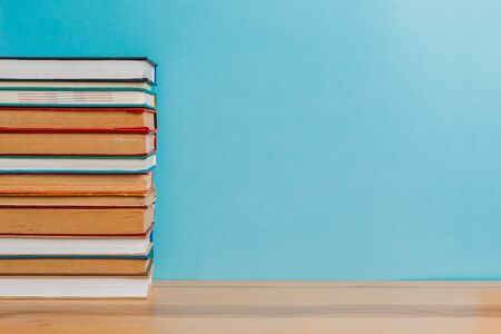 A simple composition of many hardback books, raw books on a wooden table and a bright blue background. back to school. Education.の写真素材