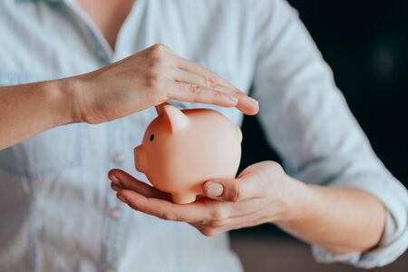 Woman holding a pink piggy bank, copy space next to her. Concept of saving money or savingsの写真素材