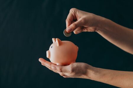 female hands puts a coin in a pink piggy bank. The concept of saving money or savings, investmentの写真素材