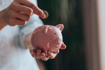 female hands puts a coin in a pink piggy bank. The concept of saving money or savings, investmentの写真素材