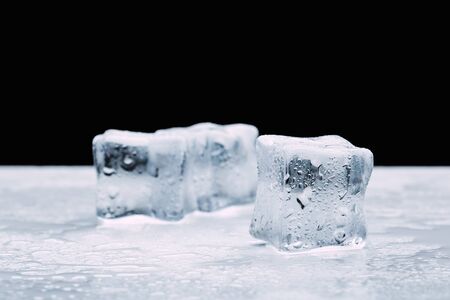 several melted ice cubes with drops on a dark black background