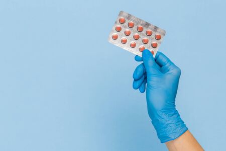 Doctor's hand in a blue medical glove holds a blister of pills on a blue background. Treatment