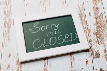 Sign "Sorry, we are closed" on a chalk board with English inscriptions on a wooden background. Closed business or store concept.の写真素材