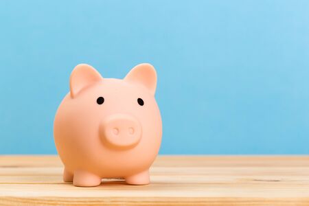 Pink piggy bank on wooden table and blue background. The concept of storage, accumulation. Crisis, inflation, financial collapse.の写真素材