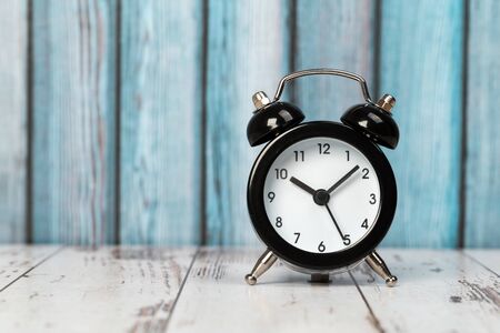 Black retro alarm clock with bells on a wooden table, daily routine concept. ten hours 10 minutes