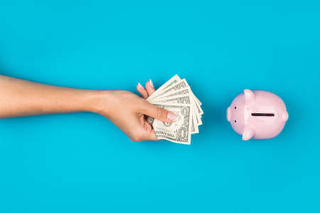 female hands put money in a piggy bank on a blue background. . Retirement retention