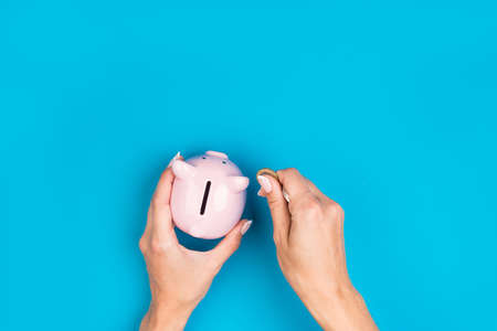 female hands put money in a piggy bank on a blue background. . Retirement retention