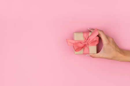 Top view of female hands holding present box package in palms on pink background