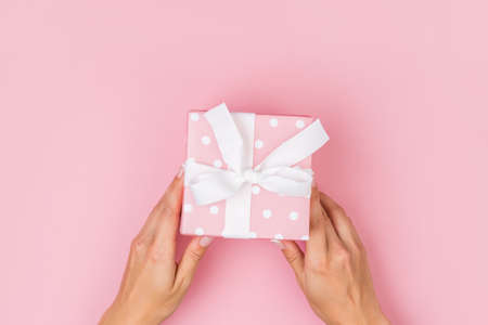 Top view of female hands holding present box package in palms, on pink backgroundの写真素材