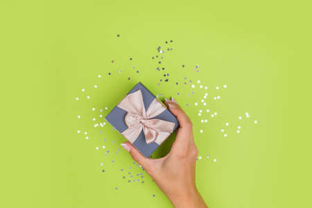 Women hands holding a gift or gift box decorated with confetti on a green table top view.