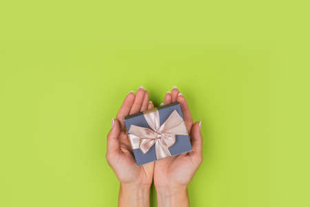 Hands holding crafts paper gift box with a gift for Christmas, New Year, Valentine's Day or anniversary on a green background, top viewの写真素材