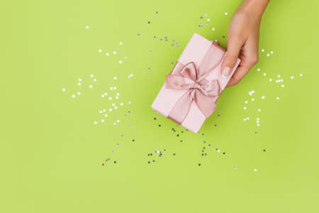 Women hands holding a gift or gift box decorated with confetti on a green table top view.の写真素材