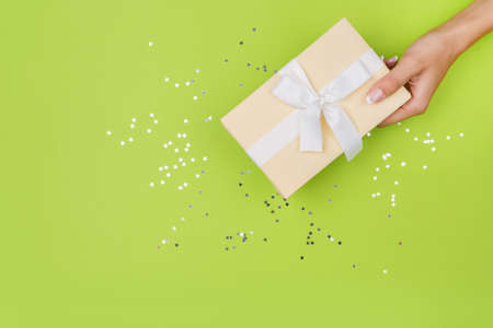 Women hands holding a gift or gift box decorated with confetti on a green table top view.の写真素材