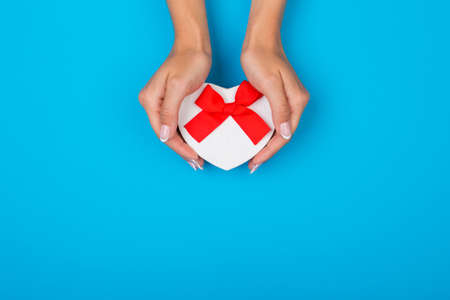 Hands holding craft paper gift box with a present for Christmas, New Year, Valentine's Day or anniversary on a blue background, top viewの写真素材