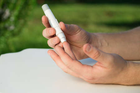 Man taking a blood sample with a lancet handle outside against the backdrop of greenery. Diabetes, health care, insulin conceptの写真素材